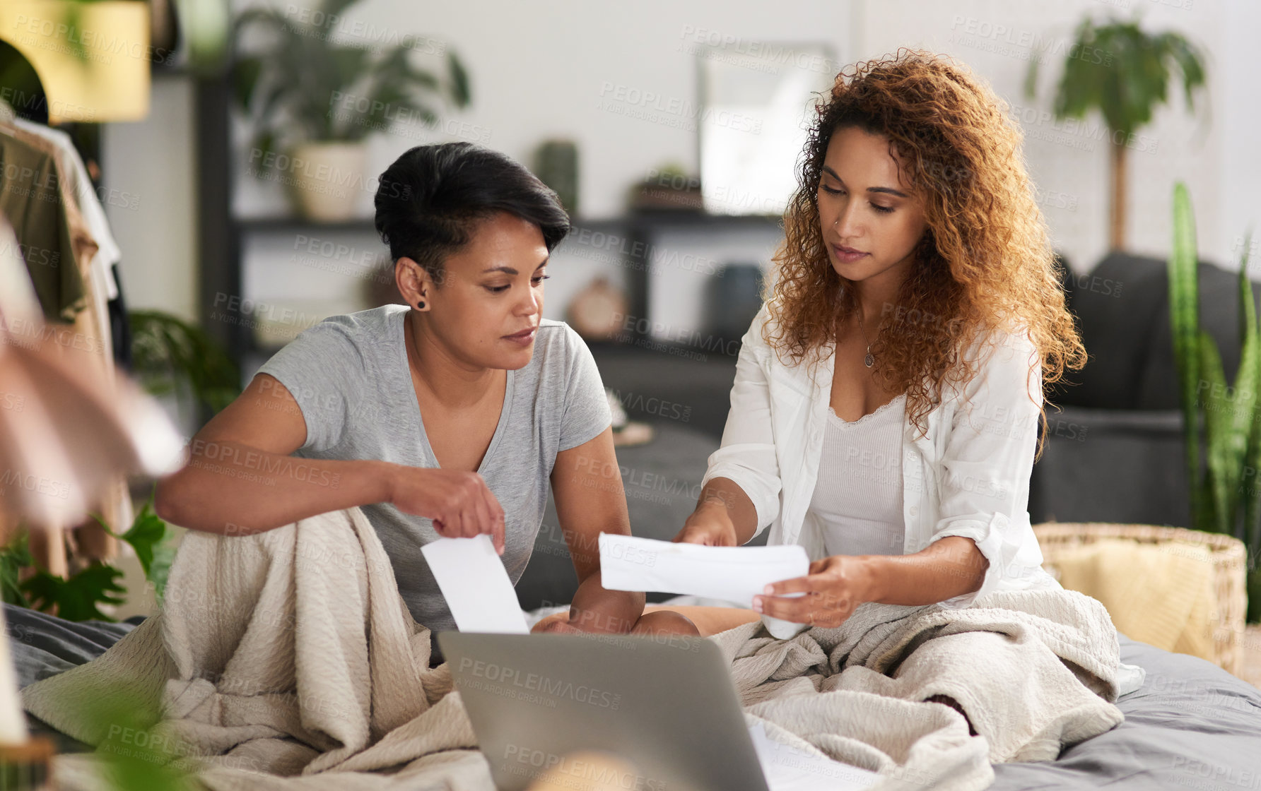 Buy stock photo Shot of a young couple holding paperwork and using a laptop while sitting at home