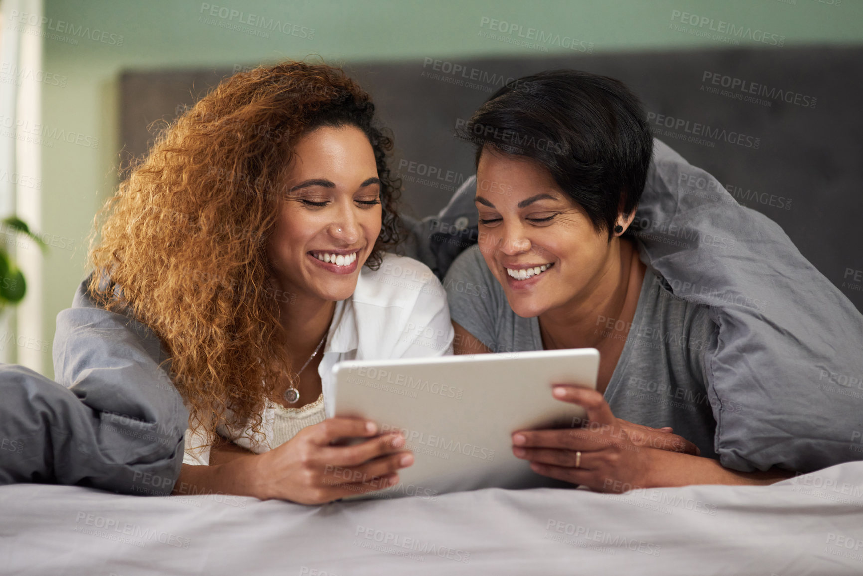 Buy stock photo Shot of a young couple using a digital tablet while lying in their bed