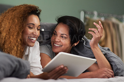 Buy stock photo Shot of a young couple using a digital tablet while lying in their bed