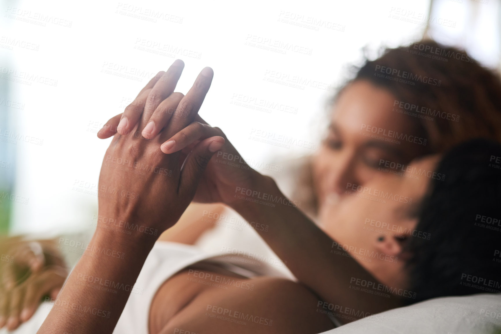 Buy stock photo Defocused shot of a young couple holding hands while lying in bed together