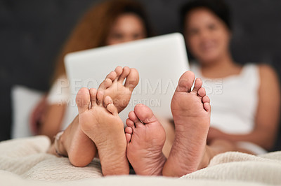 Buy stock photo Shot of a couple lying barefoot on their bed while using their laptop