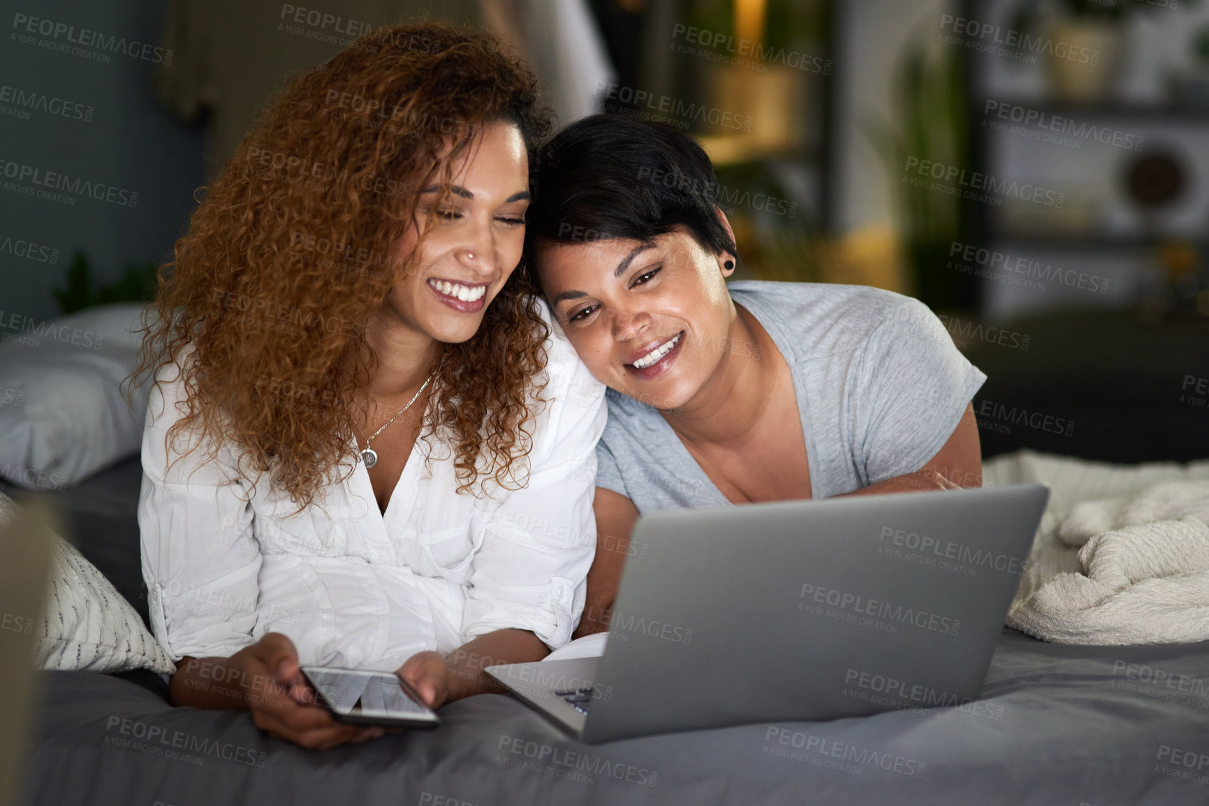 Buy stock photo Shot of a young couple using a laptop while lying on their bed