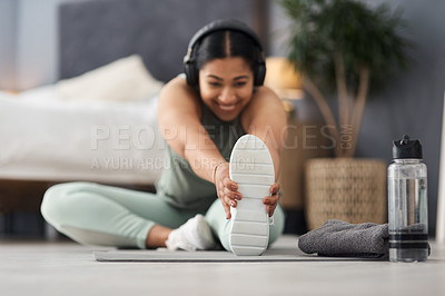 Buy stock photo Shot of a sporty young woman stretching her legs while exercising at home