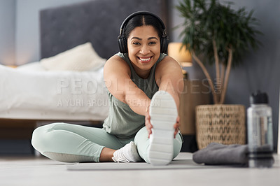 Buy stock photo Portrait of a sporty young woman stretching her legs while exercising at home