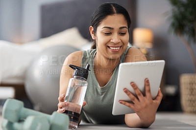 Buy stock photo Shot of a sporty young woman using a digital tablet while exercising at home