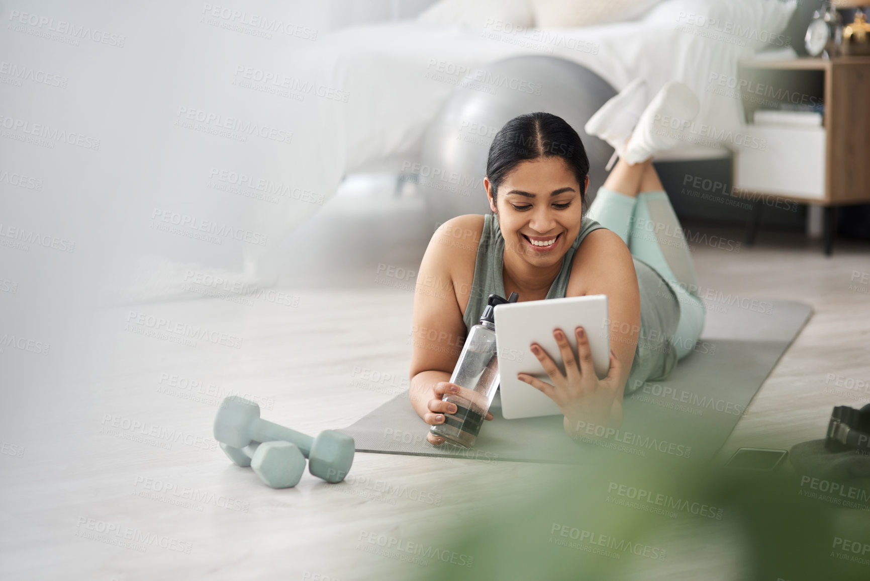 Buy stock photo Shot of a sporty young woman using a digital tablet while exercising at home