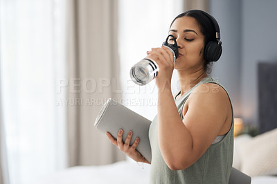 Buy stock photo Shot of a sporty young woman drinking water while exercising at home