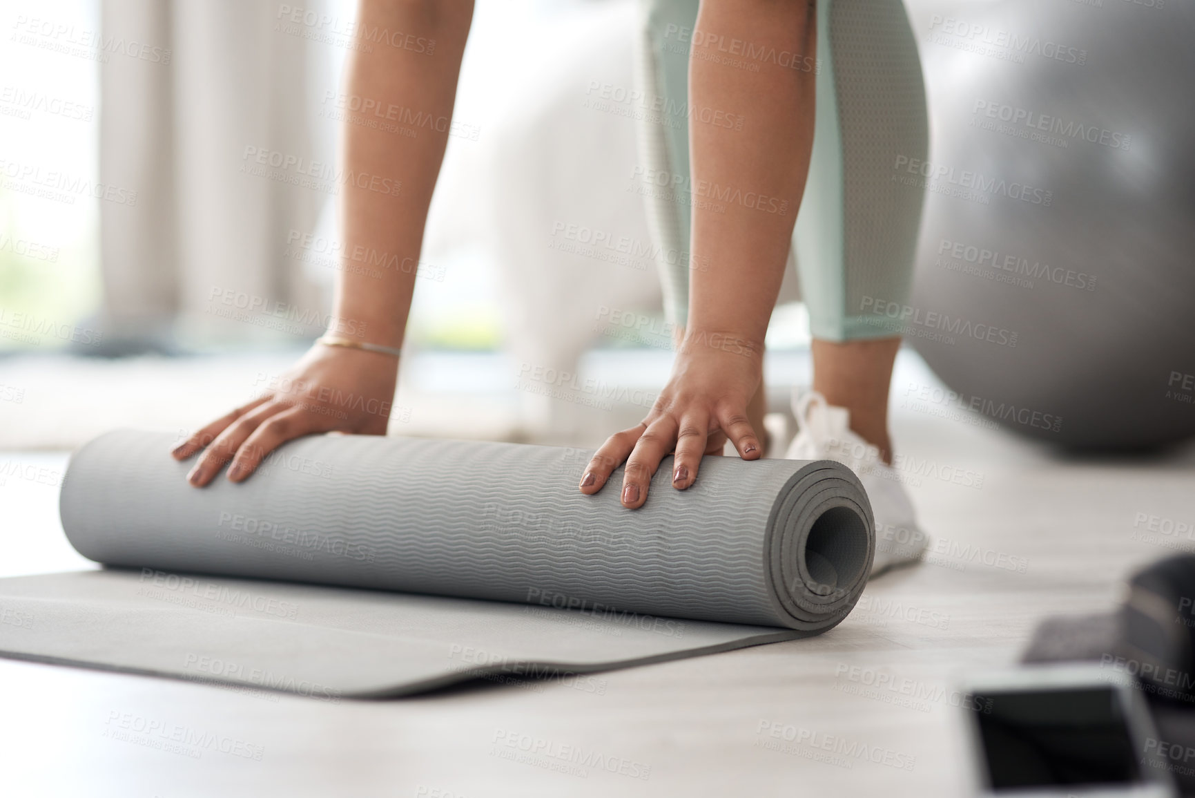 Buy stock photo Closeup shot of an unrecognisable woman rolling an exercise mat on the floor at home