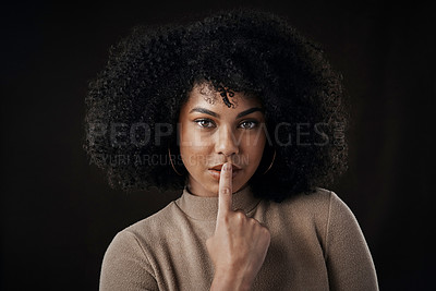 Buy stock photo Cropped portrait of an attractive young woman posing with her finger on her lips against a dark background in studio