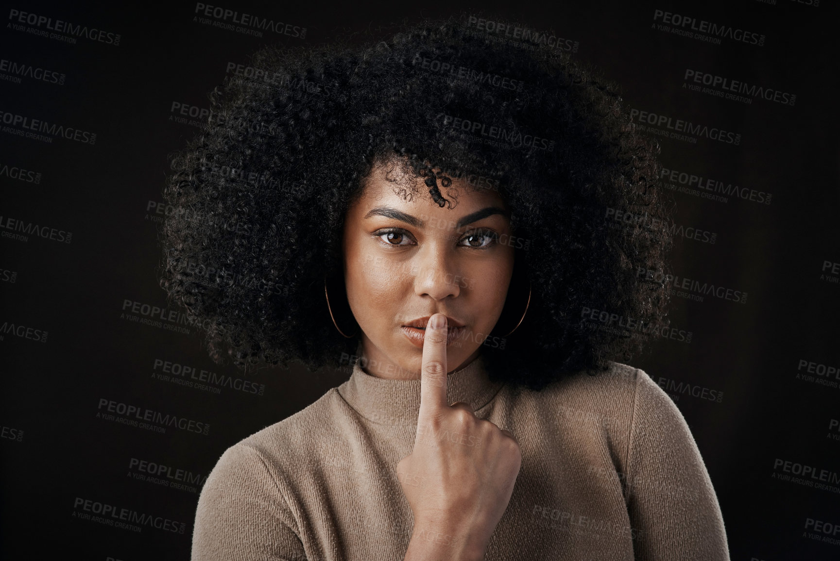 Buy stock photo Cropped portrait of an attractive young woman posing with her finger on her lips against a dark background in studio