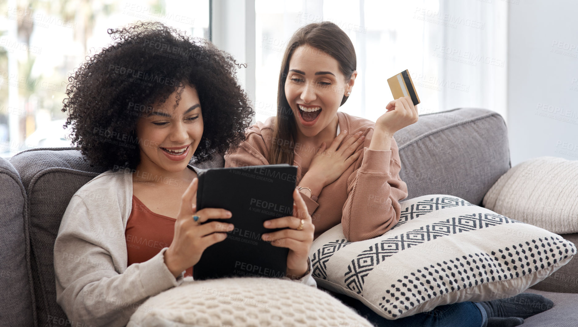 Buy stock photo Shot of two young women shopping online while sitting on the couch at home