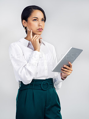 Buy stock photo Studio shot of a young businesswoman using a digital tablet and looking thoughtful against a grey background