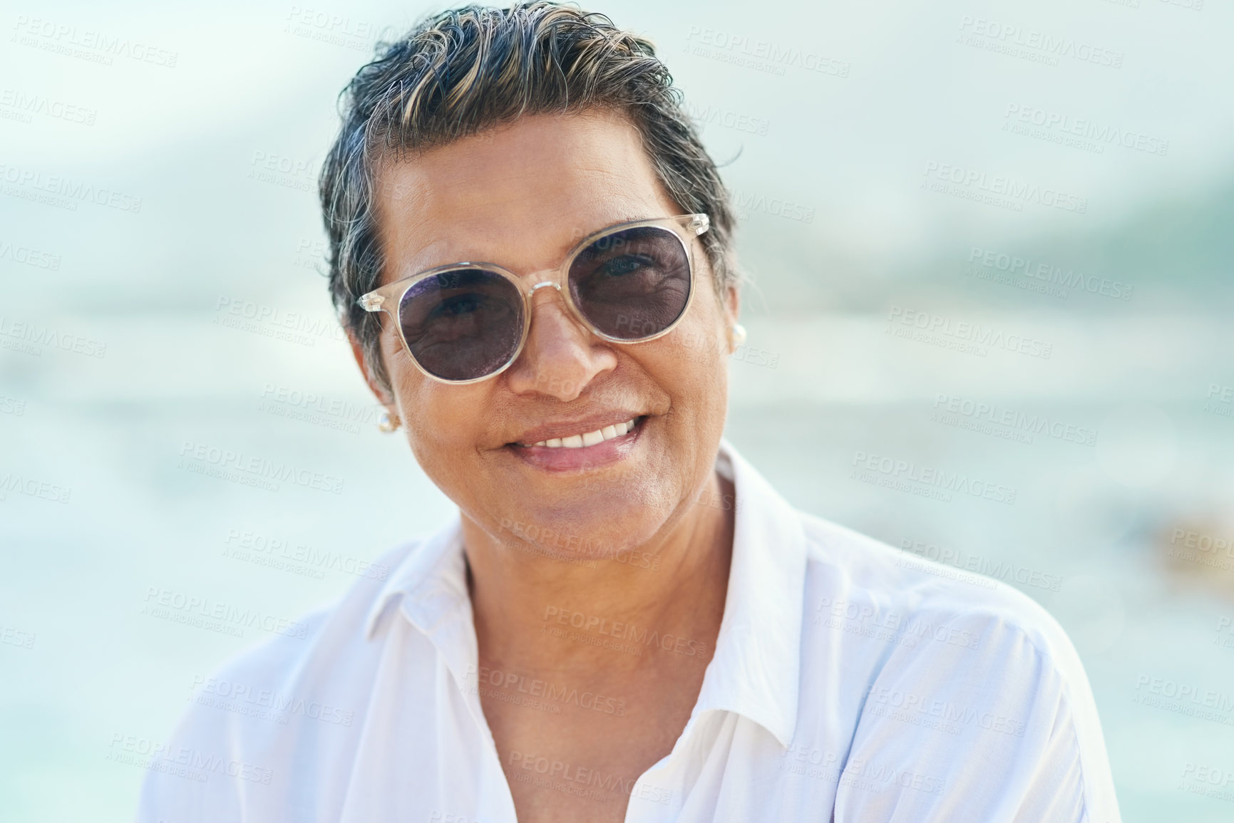 Buy stock photo Shot of an attractive mature woman standing alone during a day out on the beach