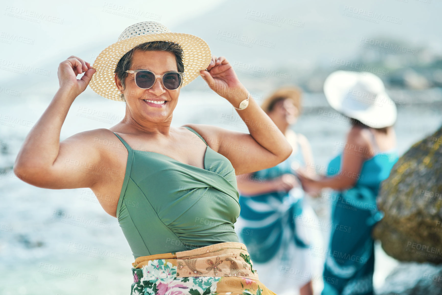 Buy stock photo Shot of an attractive mature woman standing and posing during a day out on the beach with friends