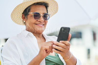 Buy stock photo Shot of a mature woman sitting alone and using her cellphone during a day out on the beach