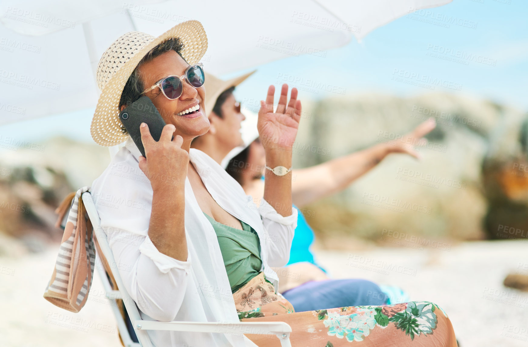 Buy stock photo Shot of a mature woman sitting alone and using her cellphone during a day out on the beach with friends