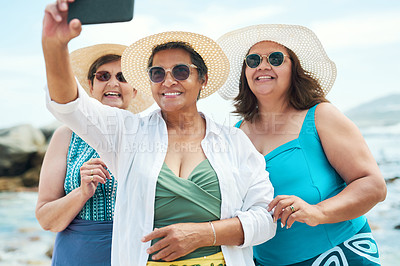 Buy stock photo Shot of a mature group of friends standing together and using a cellphone to take a selfie on the beach