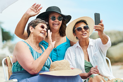 Buy stock photo Shot of a mature group of friends using a cellphone for a video chat during a day on the beach