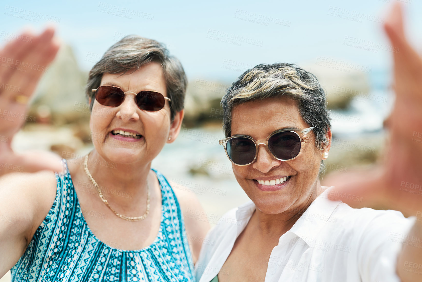 Buy stock photo Shot of two mature friends standing together and posing for a selfie during a day out on the beach