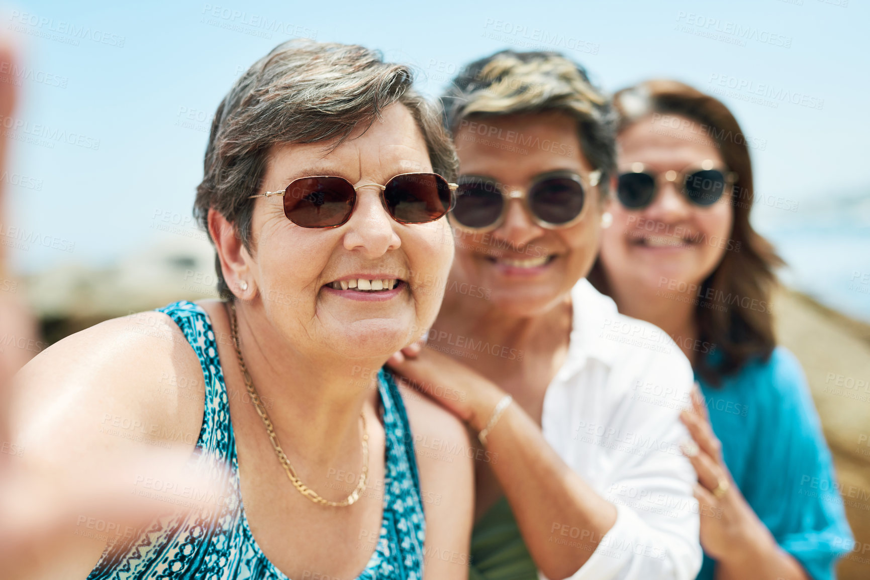 Buy stock photo Shot of a mature group of friends standing together and posing for a selfie during a day on the beach