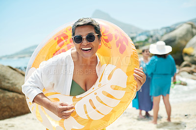 Buy stock photo Shot of a mature woman standing and holding a pool inflatable during a day on the beach with friends