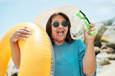 Buy stock photo Shot of a mature woman standing and holding a pool inflatable and snorkel during a day on the beach