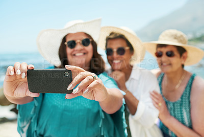 Buy stock photo Shot of a mature group of friends standing together and using a cellphone to take a selfie on the beach