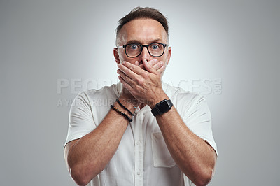 Buy stock photo Studio portrait of a mature man covering his mouth and looking shocked against a grey background