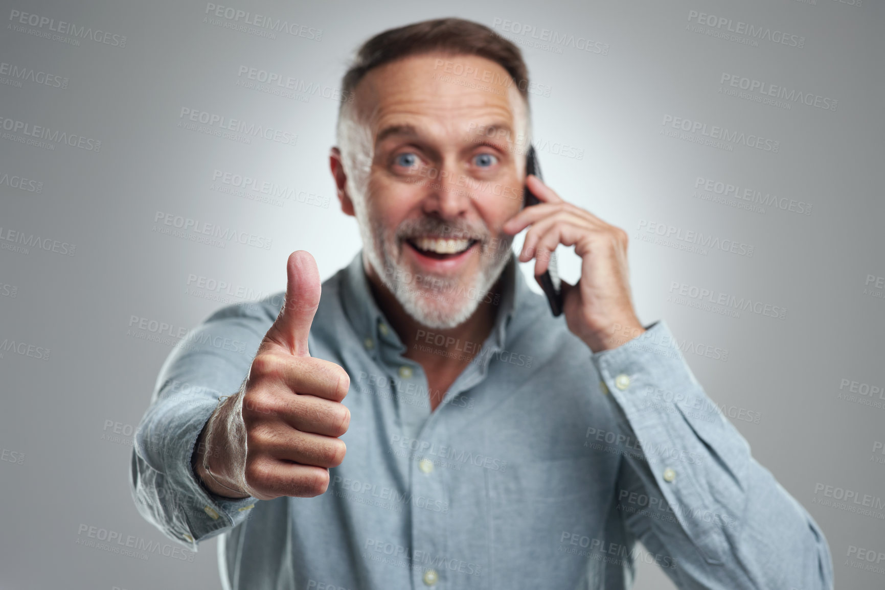 Buy stock photo Studio portrait of a mature man showing thumbs up while talking on a cellphone against a grey background