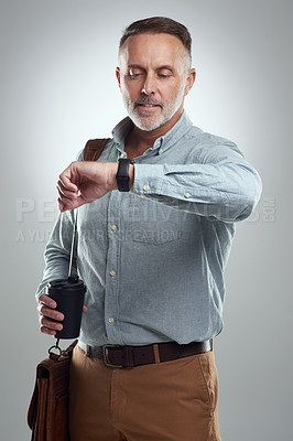 Buy stock photo Studio shot of a mature man carrying a bag and cup of coffee while the time on his wristwatch against a grey background