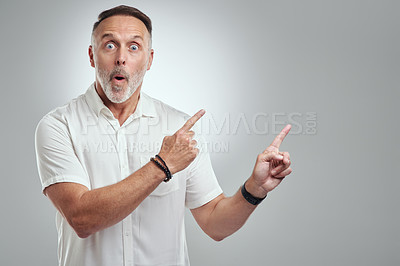 Buy stock photo Studio portrait of a mature man pointing to copyspace against a grey background