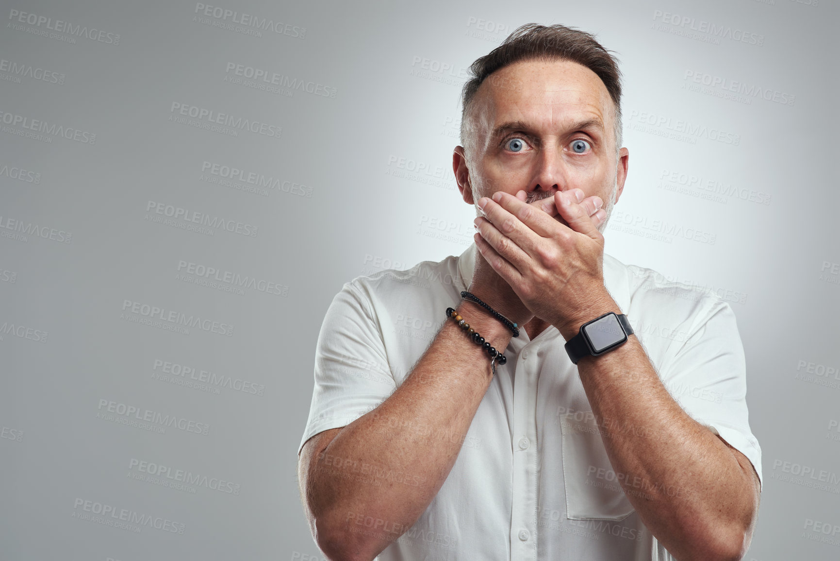 Buy stock photo Studio portrait of a mature man covering his mouth and looking shocked against a grey background