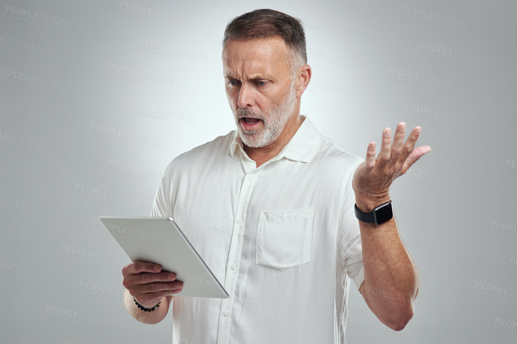 Buy stock photo Studio shot of a mature man looking confused while using a digital tablet against a grey background