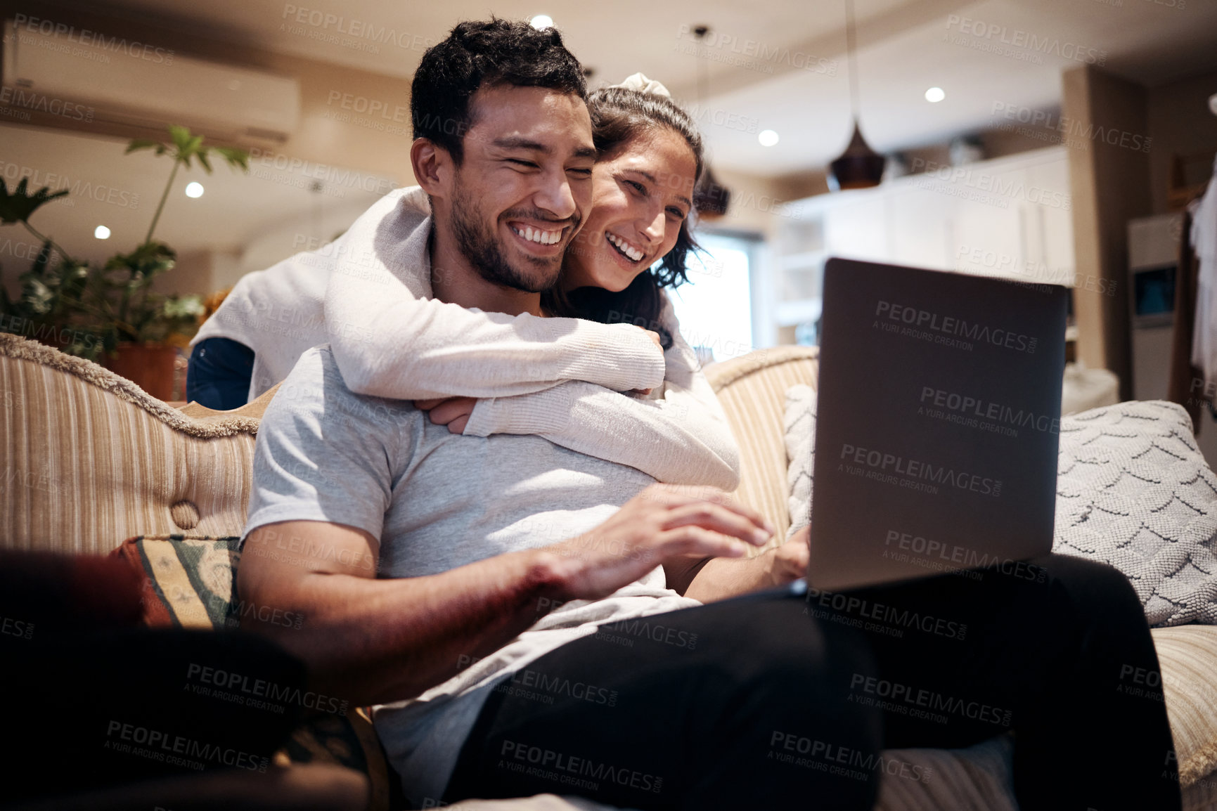 Buy stock photo Shot of a man using his laptop while his girlfriend embraces him from behind