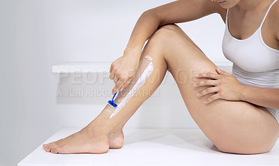 Buy stock photo Cropped shot of an unrecognizable woman sitting down and shaving her legs at home
