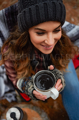 Buy stock photo High angle shot of a young woman drinking a warm beverage while camping in the wilderness during winter