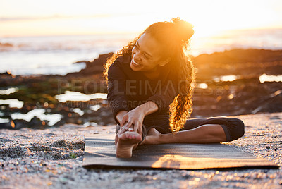 Buy stock photo Shot of an attractive young woman sitting on a mat and stretching while doing yoga on the beach at sunset