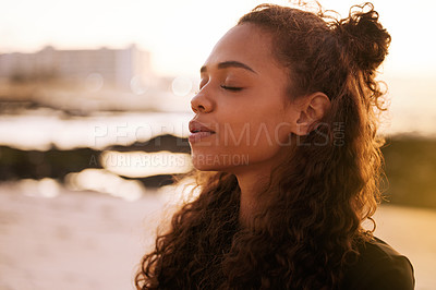 Buy stock photo Shot of an attractive young woman sitting alone on a mat and meditating on the beach at sunset