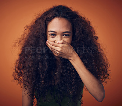 Buy stock photo Shot of a woman with curly hair covering her mouth while laughing against an orange background