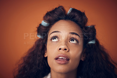 Buy stock photo Shot of a woman wearing hair rollers while standing against an orange background