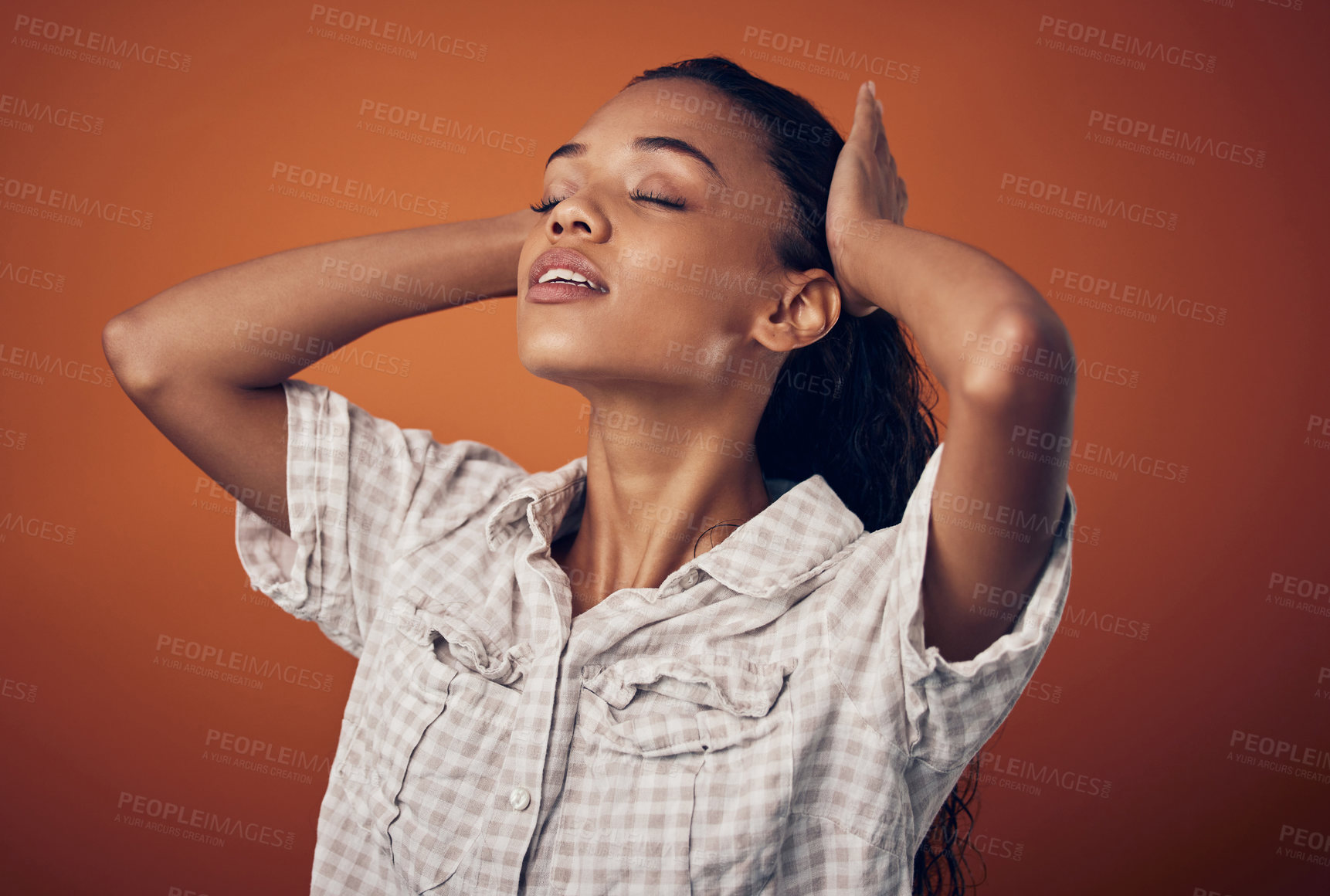 Buy stock photo Shot of a woman stroking her wet hair against an orange background