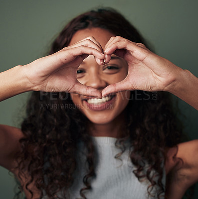 Buy stock photo Studio shot of a young woman making a heart shaped gesture against a green background