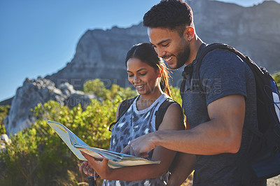 Buy stock photo Shot of a young couple using a guide book to complete a hike in a mountain range