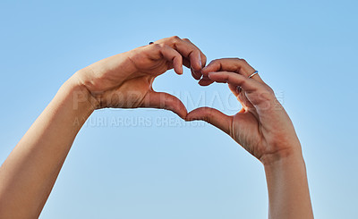 Buy stock photo Cropped shot of a woman forming a heart shape with her hands against a blue sky