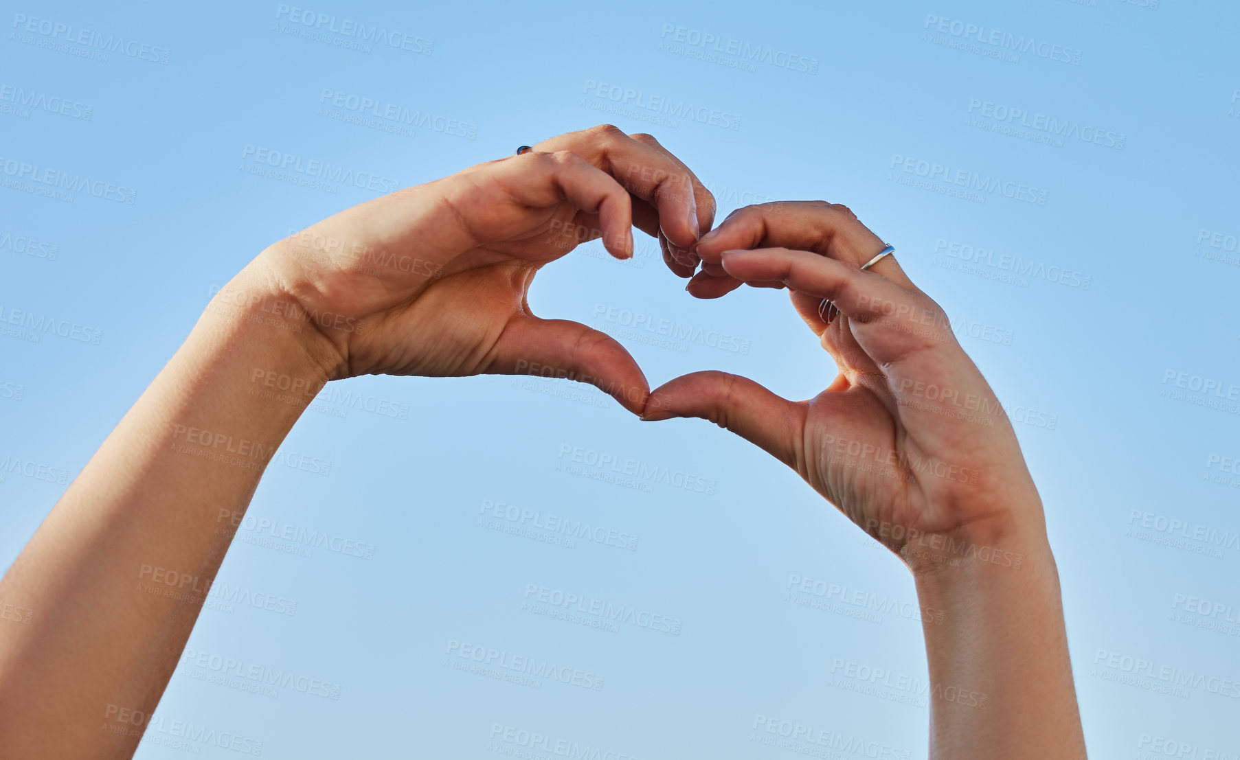 Buy stock photo Cropped shot of a woman forming a heart shape with her hands against a blue sky