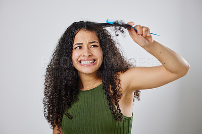 Buy stock photo Shot of a woman frowning while combing her hair against a grey background