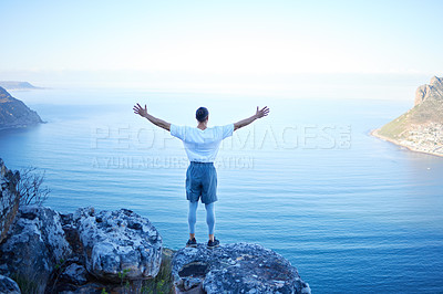 Buy stock photo Rearview shot of an unrecognizable young man standing with his arms outstretched while looking at the ocean view from the mountain