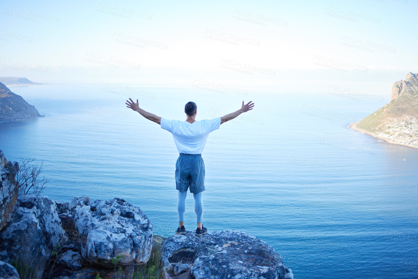 Buy stock photo Rearview shot of an unrecognizable young man standing with his arms outstretched while looking at the ocean view from the mountain