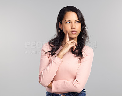 Buy stock photo Shot of a beautiful young woman looking thoughtful while standing against a grey background