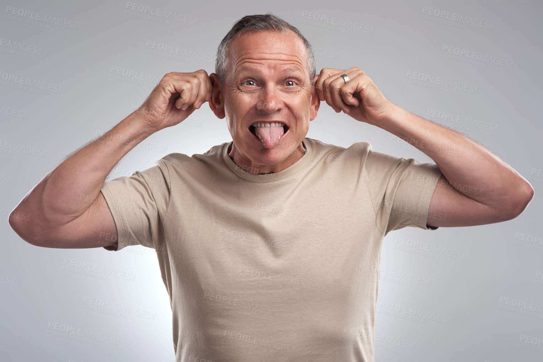 Buy stock photo Shot of a handsome mature man standing alone against a grey background in the studio and making funny faces